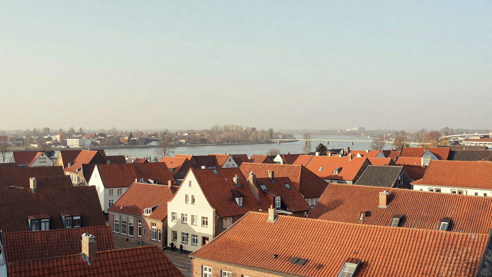 Symbolbild, KI-generiert: Blick über rote Dächer auf einen Fluss